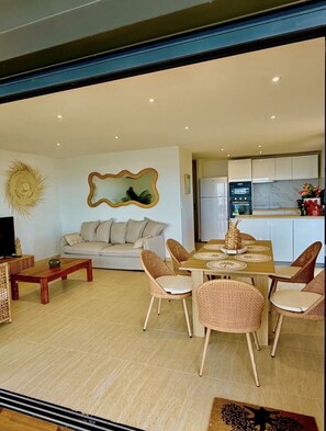 A modern living room with a sofa, dining table, and chairs. There is a kitchen area with appliances and cabinets. - SEA VIEW PINEL Villa – Brand-new waterfront villa in Oyster Pond (Oyster Pond)