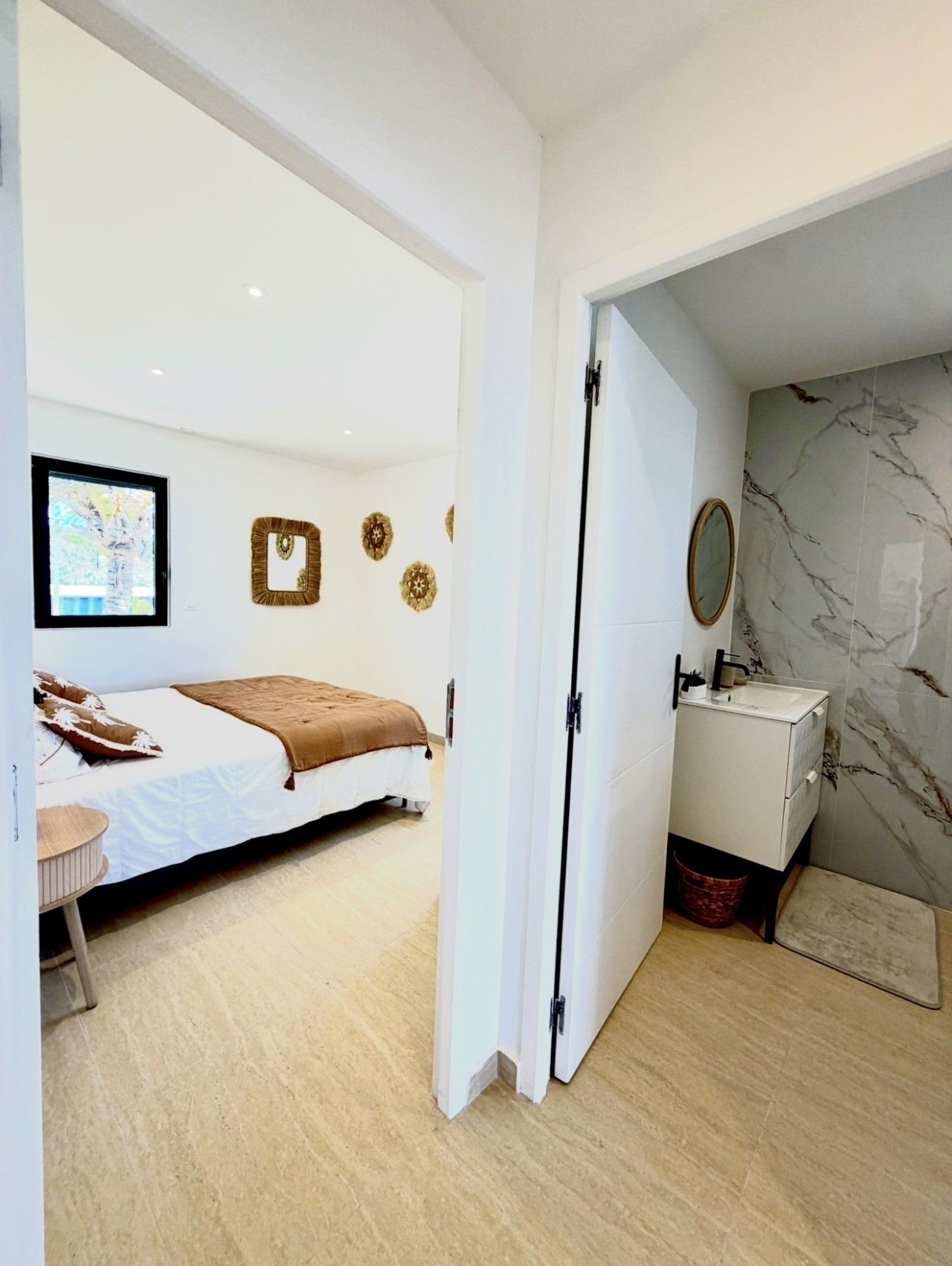 Une chambre à coucher comprenant un lit, une table de chevet, un miroir et une salle de bain avec un lavabo et un mur en marbre.