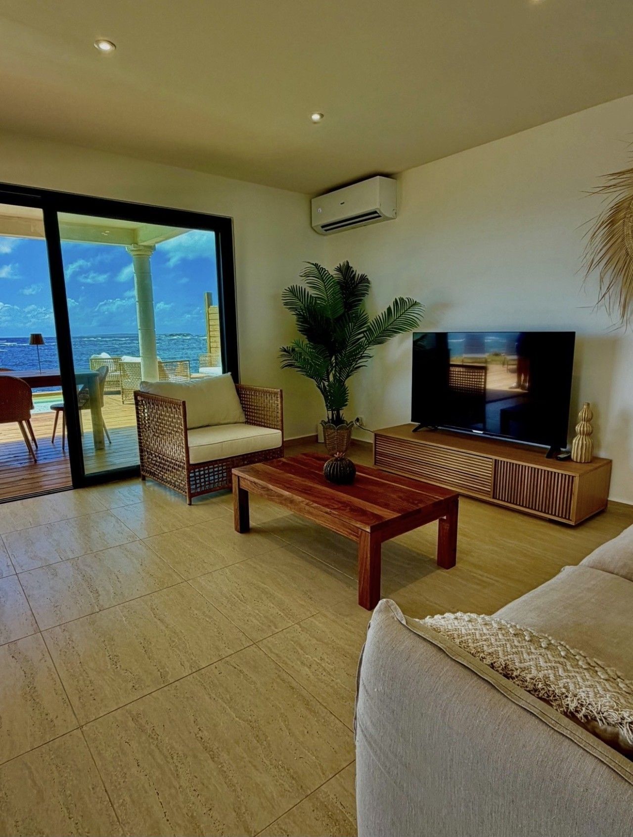Un amplio salón con un televisor grande, asientos cómodos y vista al océano a través de un ventanal.