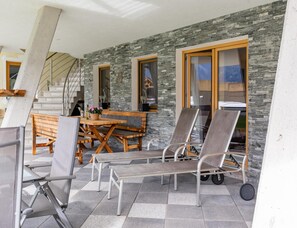 Ein überdachter Außenbereich mit einer Steinsäule, Holzmöbeln und einer Treppe zu einer erhöhten Ebene.