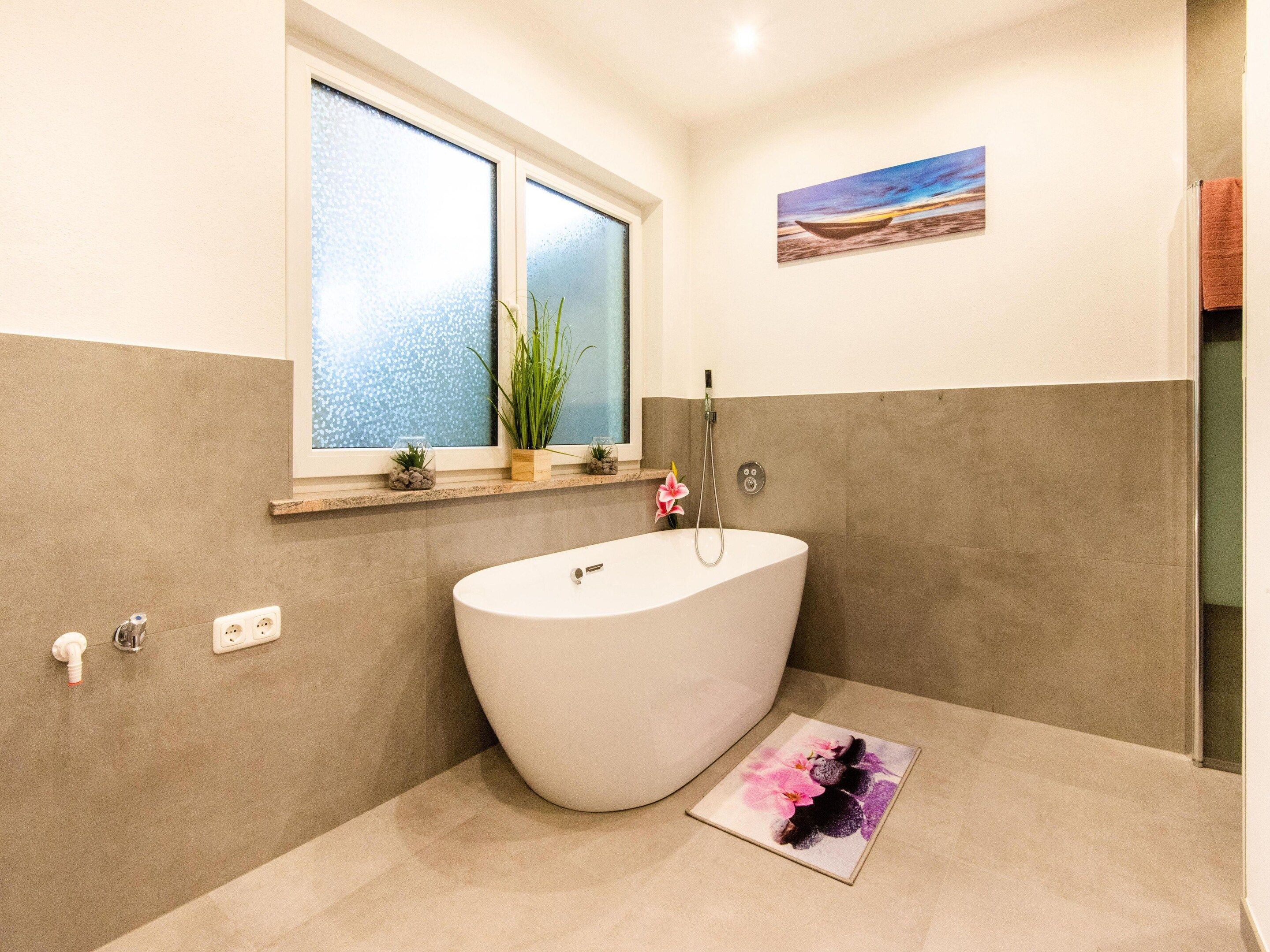 Een moderne badkamer met een vrijstaand bad, een raam met uitzicht en een klein plankje met decoratieve spullen.