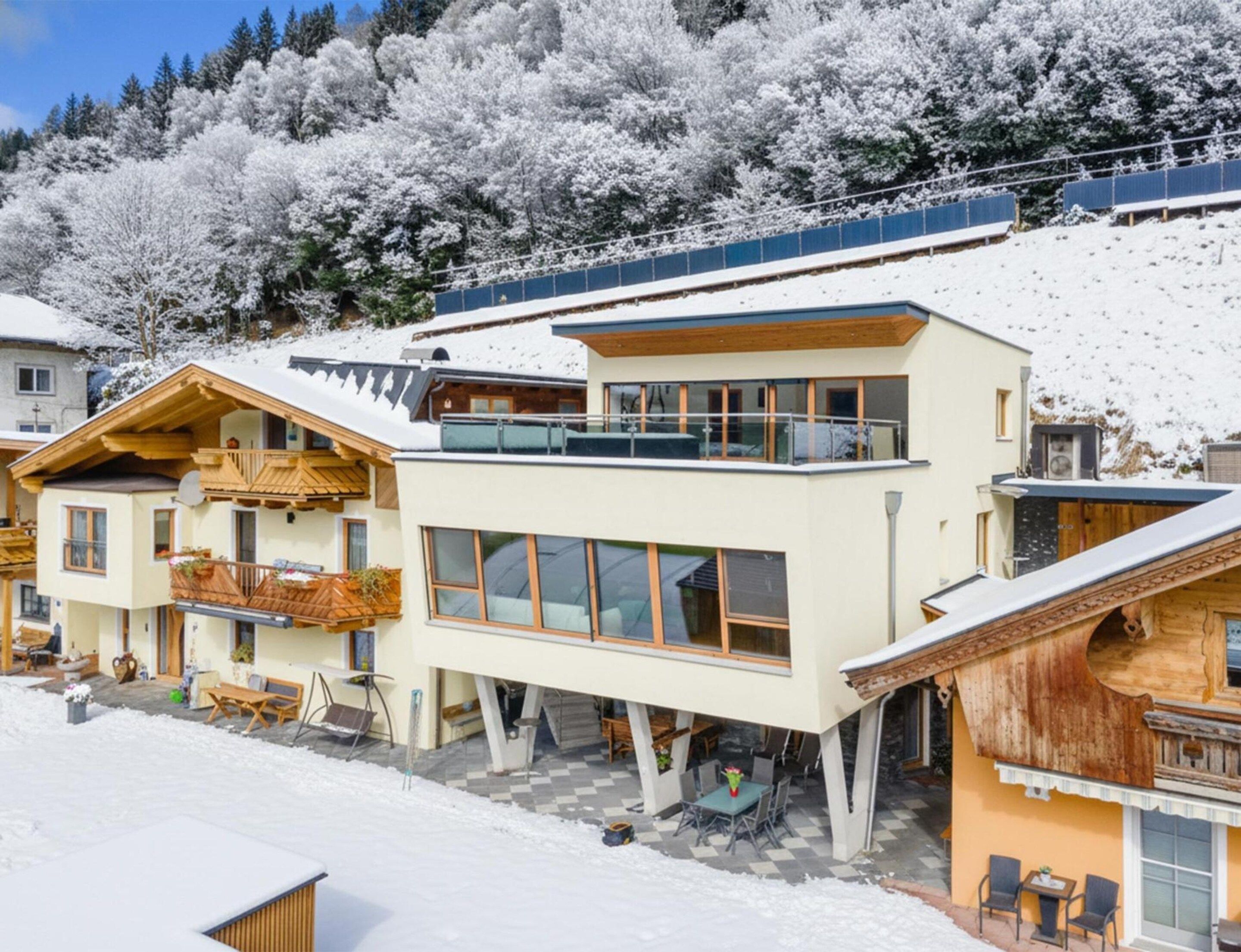 A modern ski resort with chalet-style buildings, a covered outdoor seating area, and a snowy mountain backdrop.