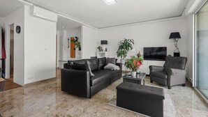 Uma sala de estar moderna com um sofá de couro preto, uma poltrona cinza, uma mesa de centro e uma televisão de tela plana.