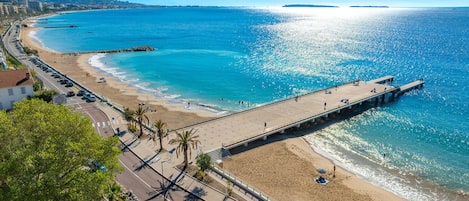 Une promenade en bord de mer, avec une jetée qui s’avance dans la mer, bordée de palmiers et une route parallèle à la plage.