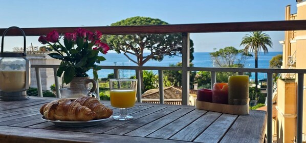 A breakfast setup with croissants, orange juice, and candles on a balcony overlooking the sea. - Chambres Privée Deux pas de la plage Cannes (Cannes)