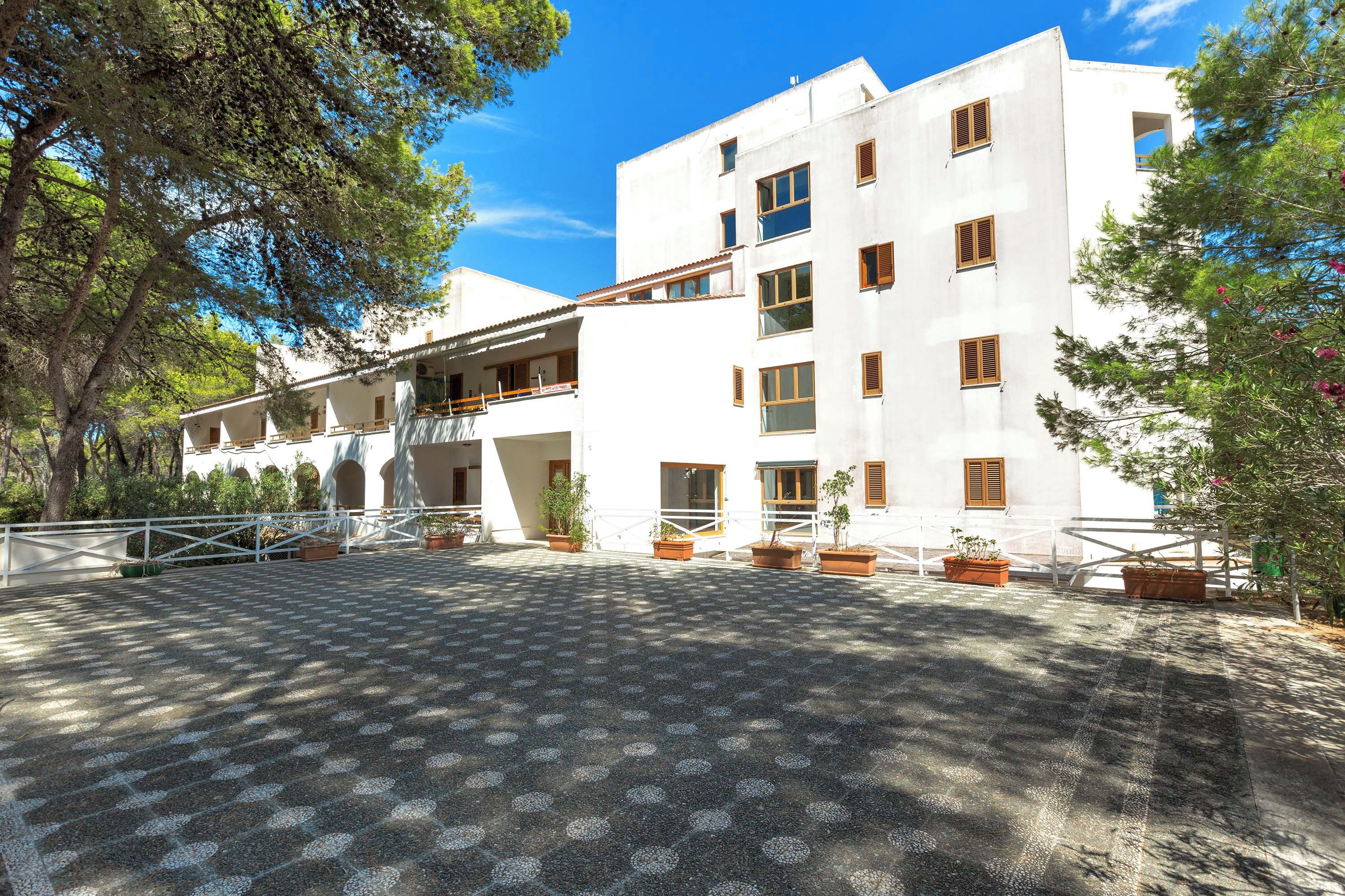 A white building with multiple floors, balconies, and potted plants.
