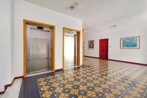 A hallway with two elevators, a patterned floor, a red door, and a framed picture on the wall. - Tra Pini e Onde by BarbarHouse (San Cataldo)
