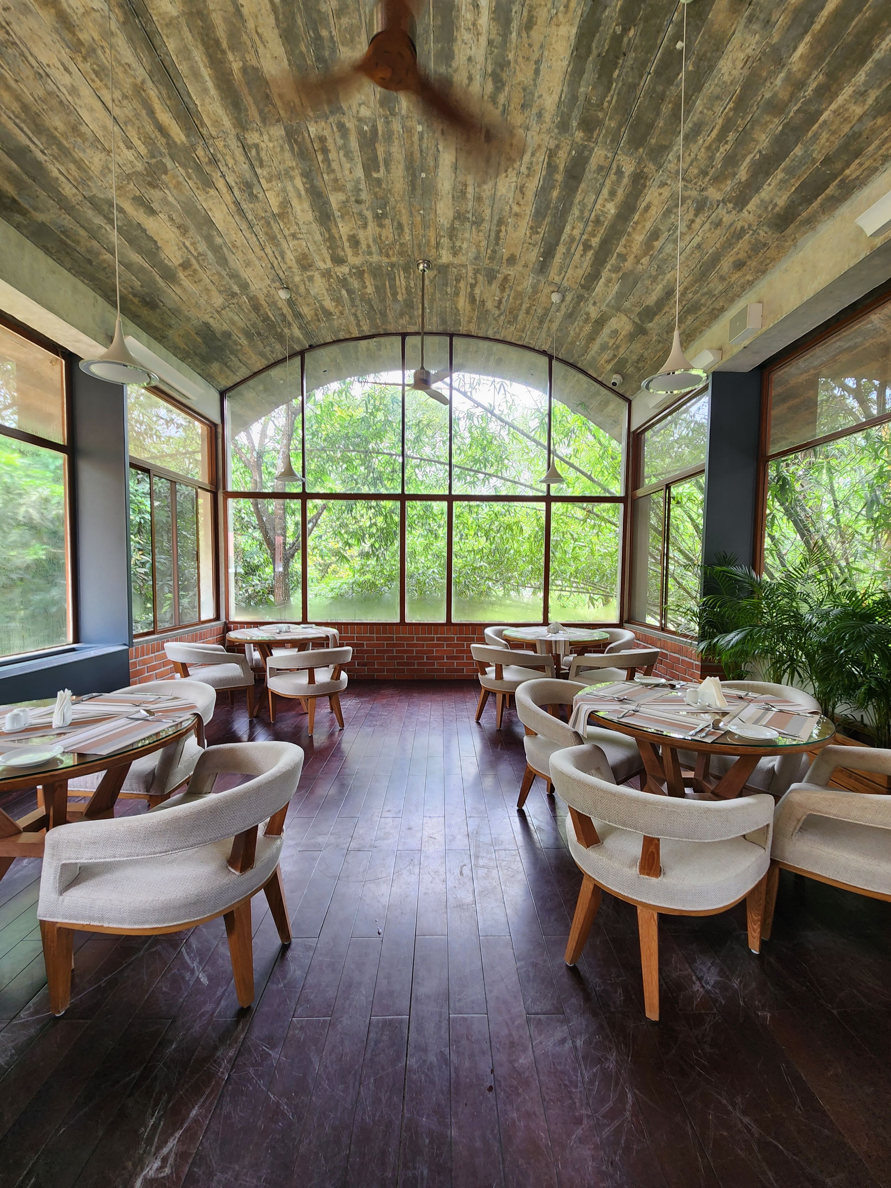 A spacious indoor area with a high ceiling, large windows, and multiple tables and chairs arranged for dining.