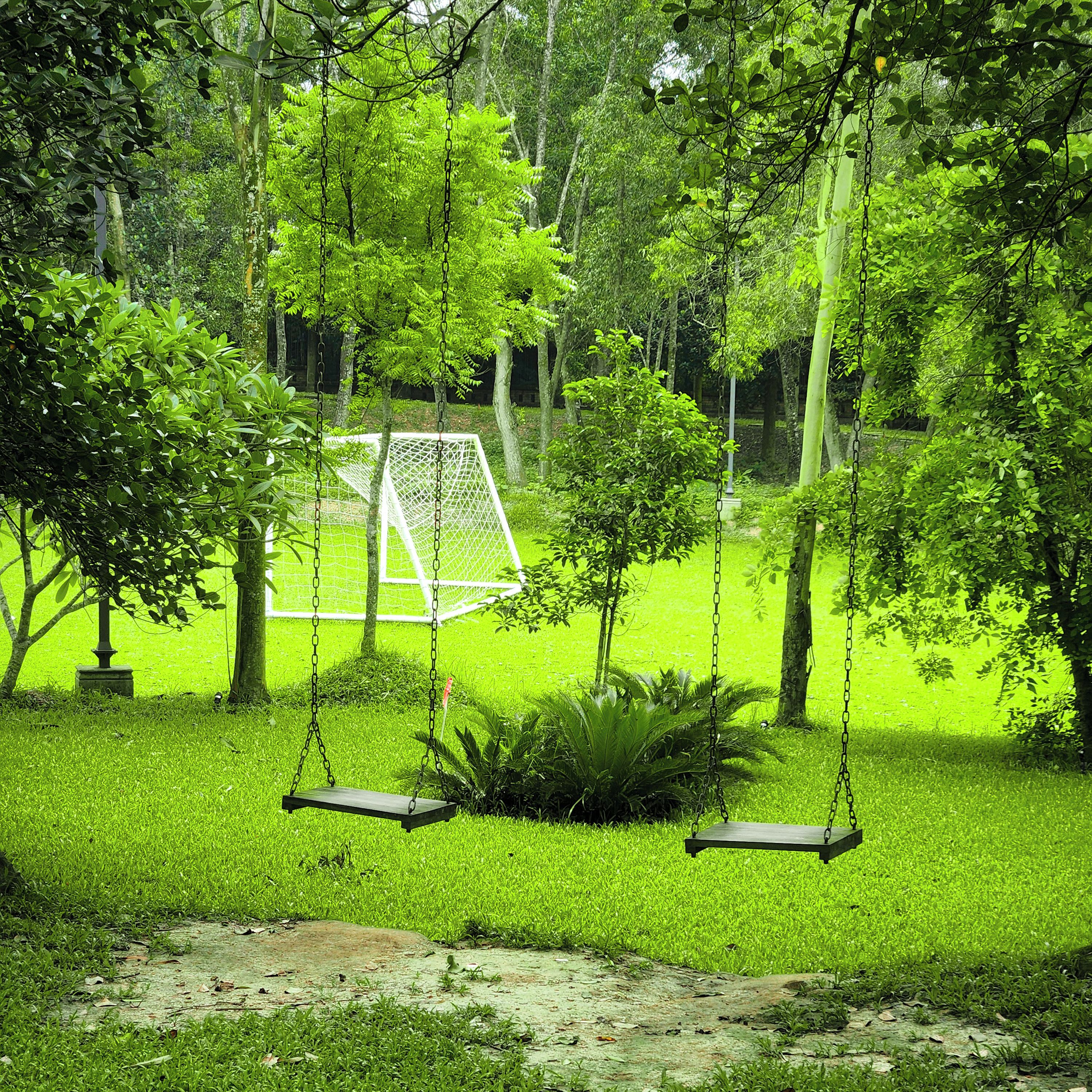 A swing set in a lush green park with a soccer goal in the background.