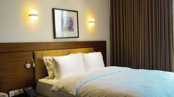 A hotel room with a bed, bedside table, lamp, and a painting on the wall.