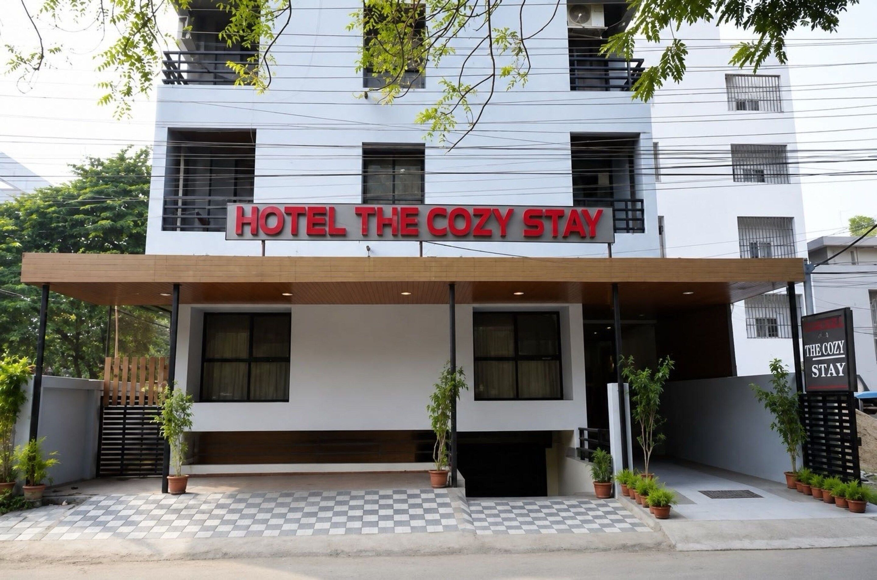 A hotel named 'Hotel The Cozy Stay' with a modern facade, large windows, and a checkered entrance.