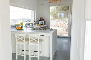 A modern kitchen with a large island, white bar stools, and a view of the outdoors. - Tranquil 3-bedroom villa with swimming pool and beautiful country views (Sicilia)