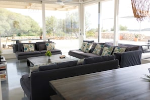 Een moderne woonkamer met een hoekbank, een salontafel en een eethoek met buitenmeubels.