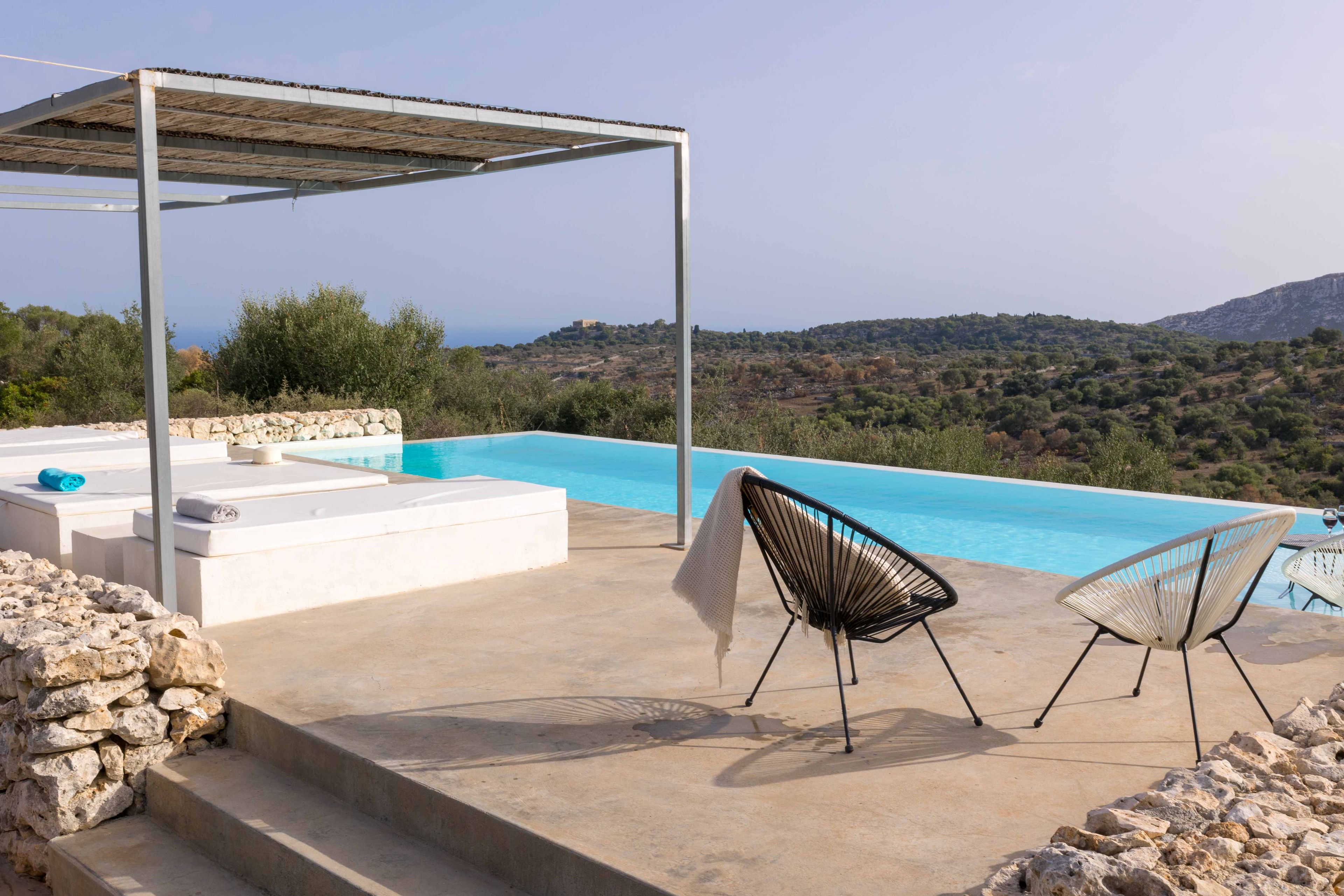 Ein Poolbereich mit einer Pergola, Liegestühlen und Blick auf die Landschaft.