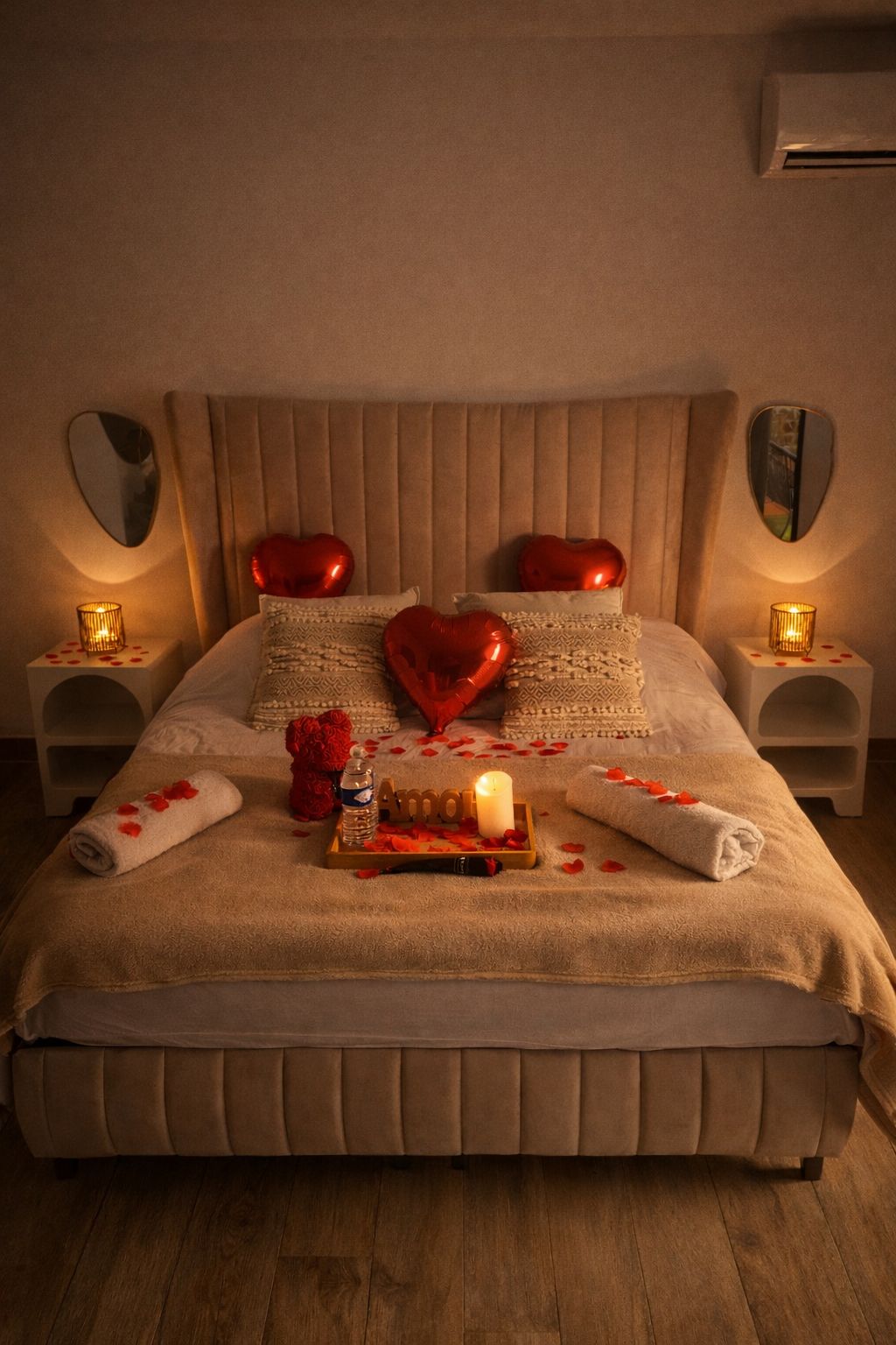 Un lit avec une tête de lit, des oreillers en forme de cœur, une bougie et un plateau avec une bouteille et un objet en forme de cœur.