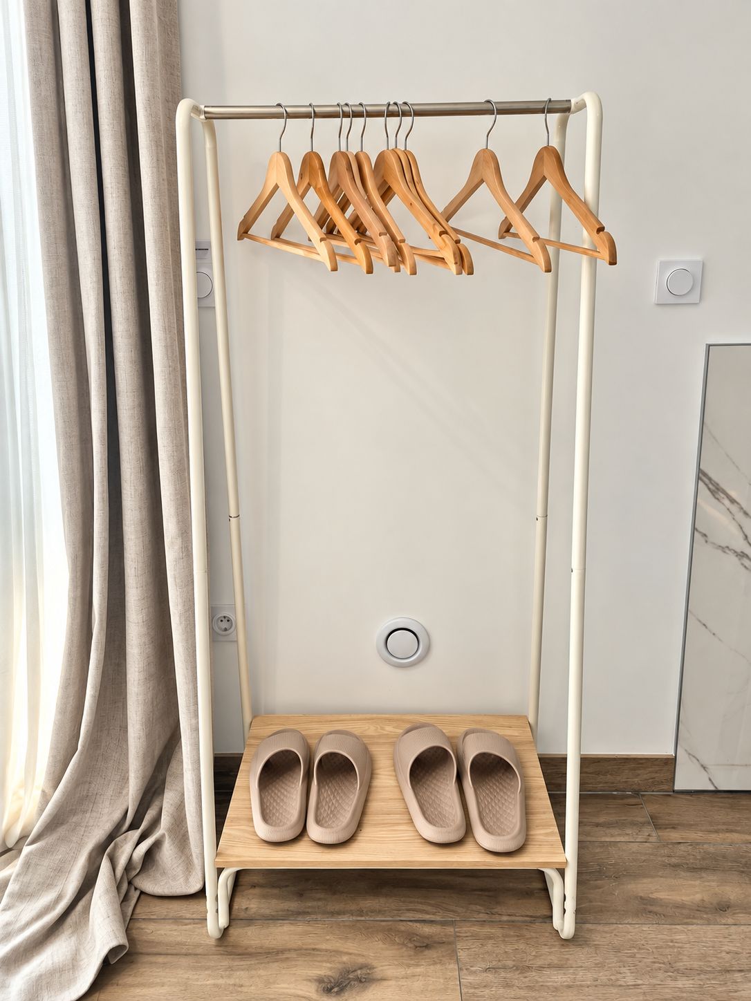 A wooden shoe rack with a white base, holding several pairs of shoes and wooden hangers.