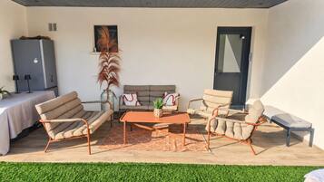 Une terrasse ensoleillée avec un canapé, des chaises et une table, une porte et une fenêtre.