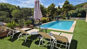 Una piscina con un área verde circundante, sillas de descanso y una mesa.