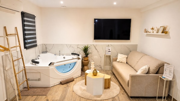 A modern bathroom with a bathtub, a wooden ladder, a marble wall, a television, and a sofa.