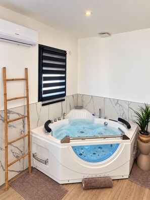 A modern bathroom with a freestanding bathtub, a wooden ladder, a black window blind, and a potted plant.