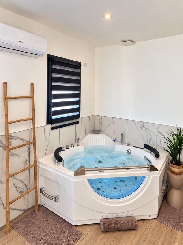 Une salle de bain moderne avec une baignoire sur pieds, une échelle en bois, un store noir et une plante en pot.