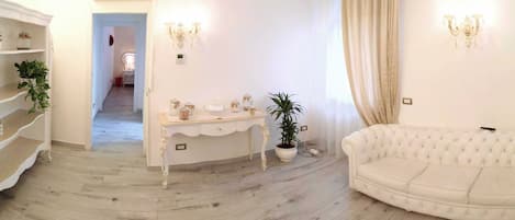 A room with a white sofa, a white console table with decorative items, a potted plant, and a staircase with a white railing.