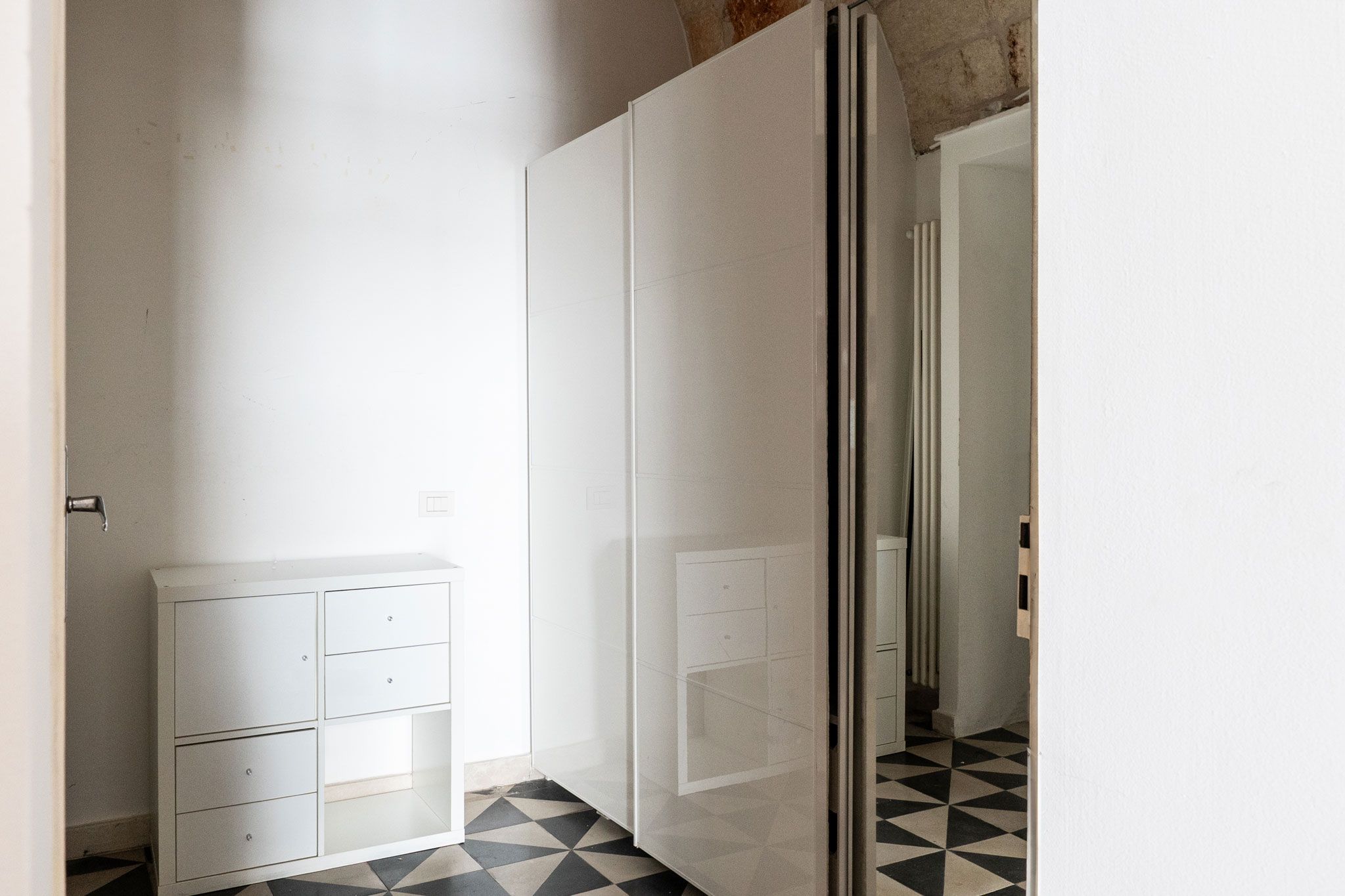 Un couloir étroit avec une armoire blanche et une porte vitrée donnant sur une autre pièce.