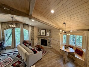 A spacious living room with a fireplace, wooden ceiling, and large windows. - Among the Pines • Minutes to Sundance (Sundance)