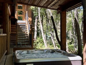 A hot tub in a wooden cabin with a staircase leading to a deck, surrounded by trees.
