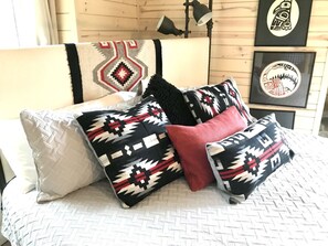 Una cama con almohadones estampados, una colcha y cuadros en la pared.