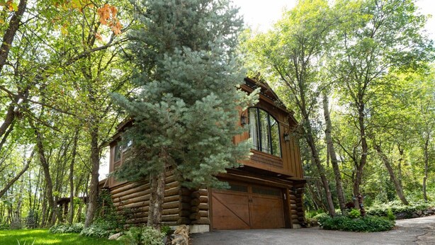 Una baita di legno con garage, immersa tra alberi e circondata da un muro in pietra.