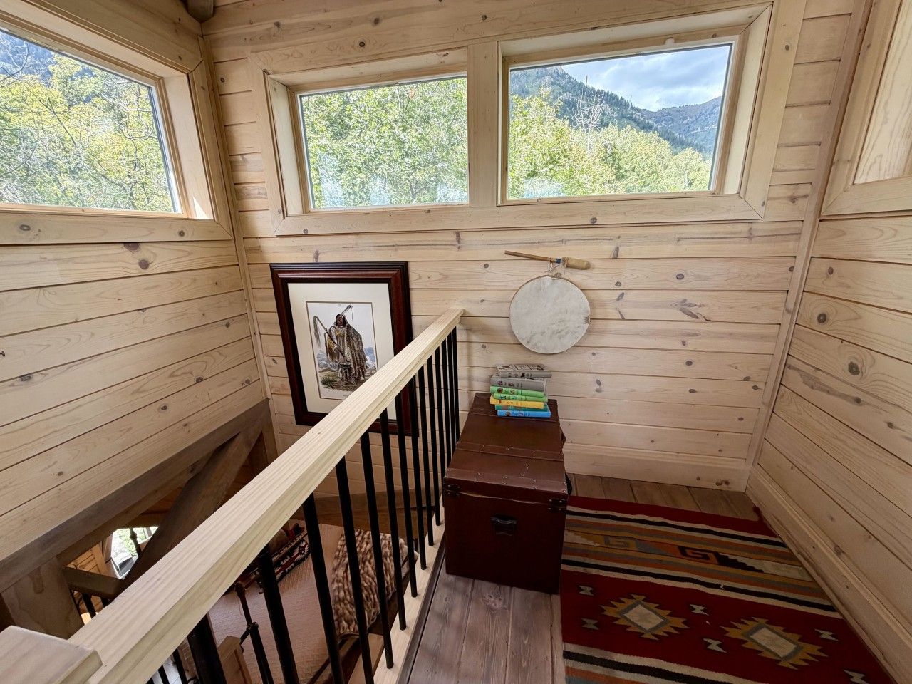 A wooden cabin interior with a staircase, a framed picture, a round table, and a rug.