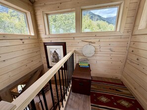 A wooden cabin interior with a staircase, a framed picture, a round table, and a rug.