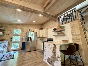 A kitchen with wooden walls, a refrigerator, a stove, and a bar area with chairs.