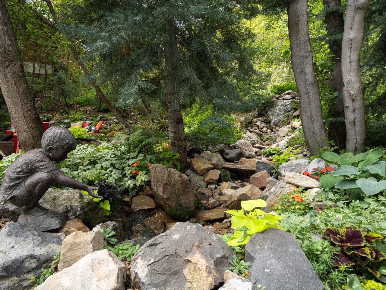 A garden with a statue of a boy, rocks, and various plants.