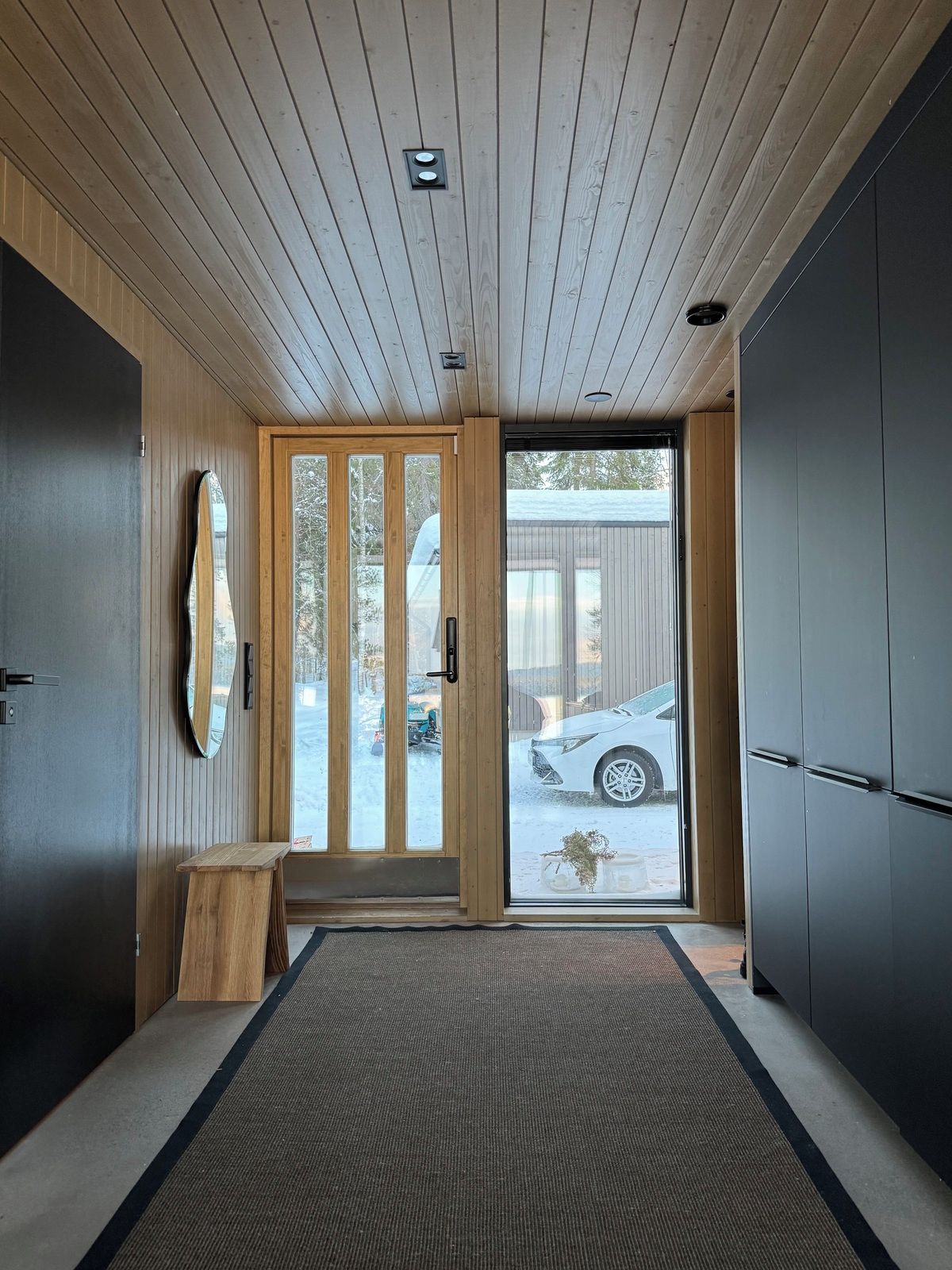 A modern interior with a wooden ceiling, a sliding glass door leading outside, and a dark-toned wardrobe.