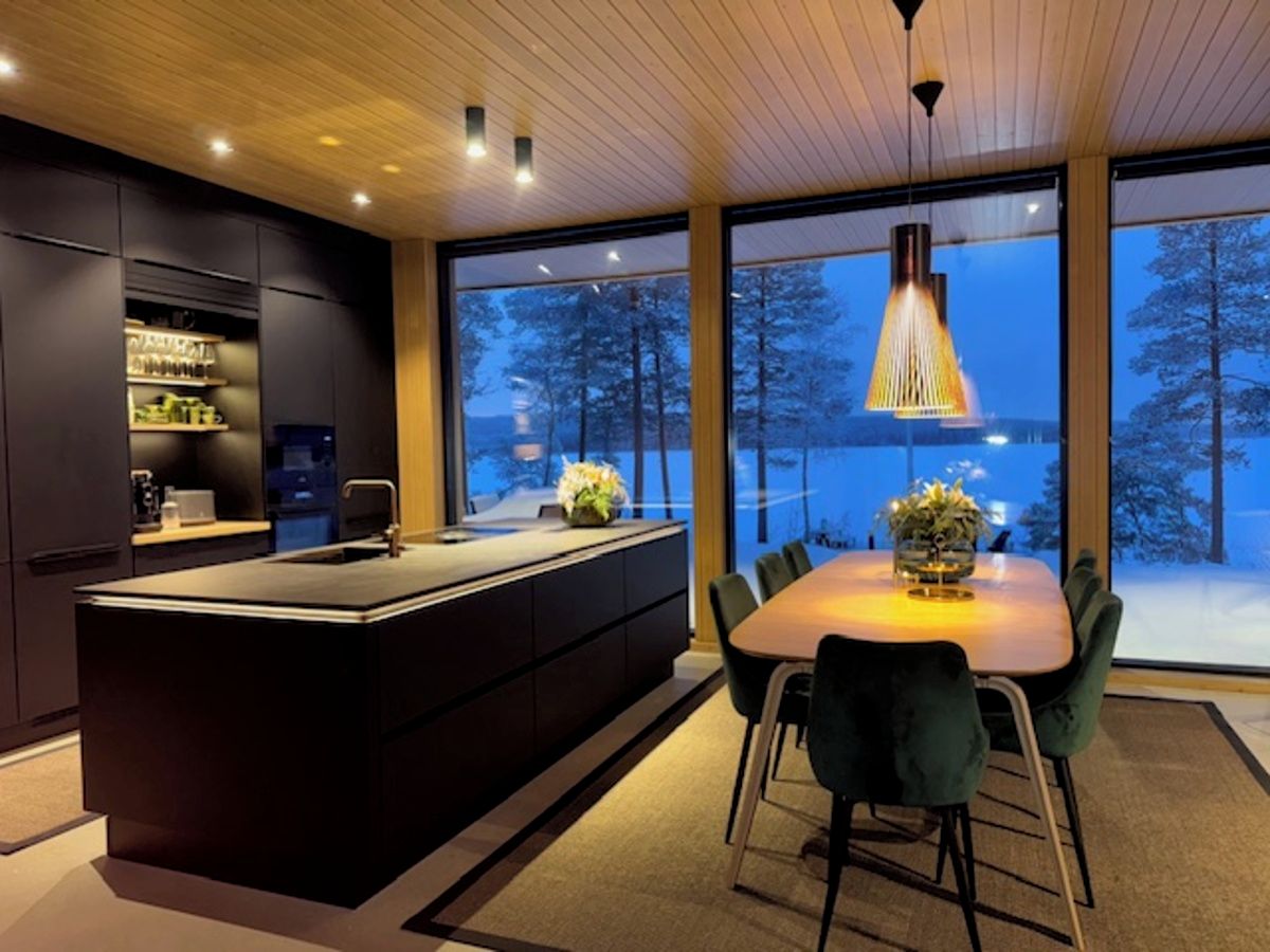 Een moderne keuken met een centraal eiland, grote ramen en een eethoek met stoelen.