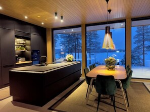 A modern kitchen with a central island, large windows, and a dining area with chairs.
