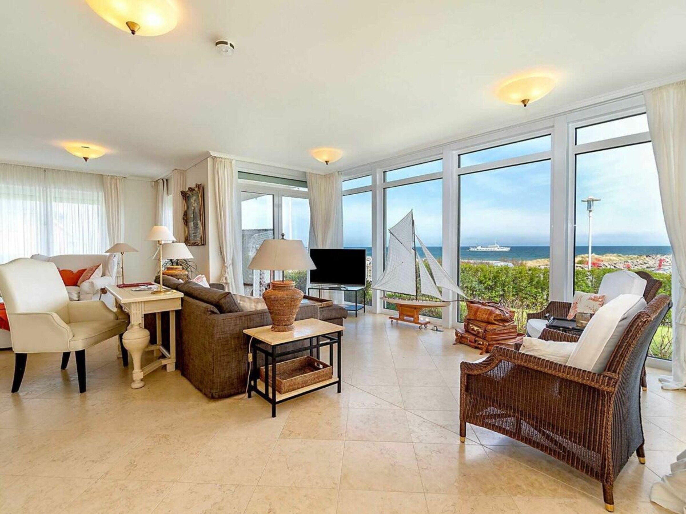 A spacious living room with a large window offering a view of the sea, a television, and comfortable seating.