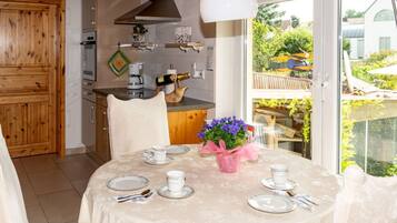 A dining area with a table set for four, a kitchen in the background, and a view of the outside.