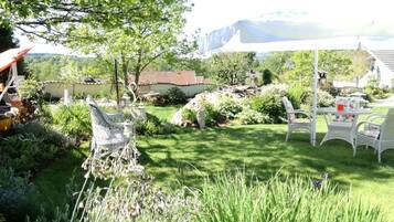 A garden with a white table and chairs, surrounded by greenery and a white umbrella.