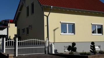 A two-story house with a red roof, white windows, and a white fence.