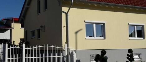 Ein zweistöckiges Haus mit rotem Dach, weißen Fenstern und einem weißen Zaun.