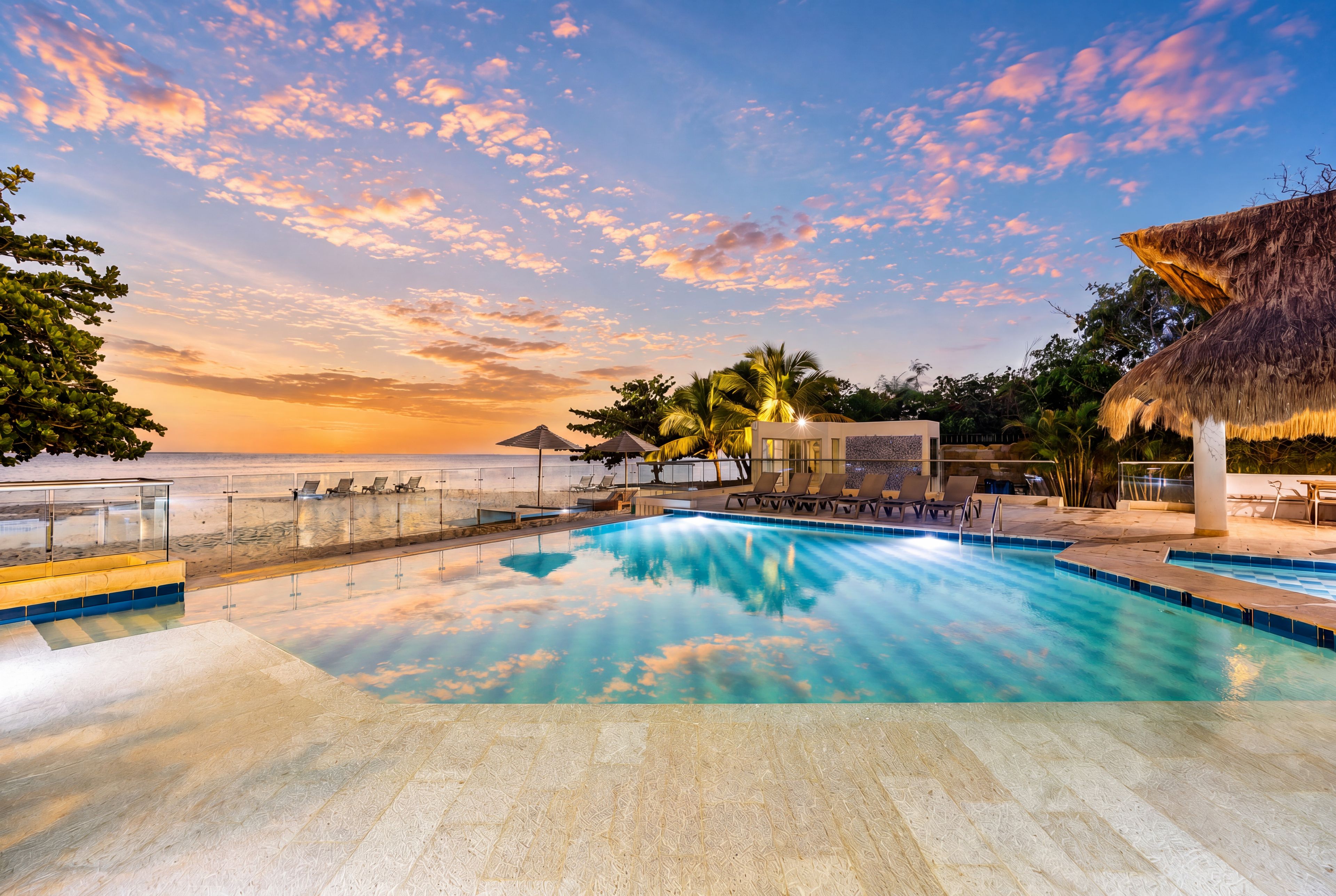 Ein Poolbereich mit Liegestühlen und Blick auf den Ozean bei Sonnenuntergang.