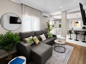 Ein modernes Wohnzimmer mit einem grauen Sofa, einem runden Couchtisch und einem an der Wand befestigten Fernseher.
