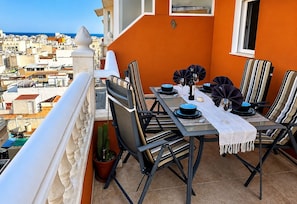 Ein Balkon mit Tisch für vier Personen, Stühlen, einem Topfpflanzen und Blick auf die Stadt.