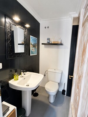 Ein modernes Badezimmer mit einem weißen Waschbecken, schwarzen Wandfliesen, einer weißen Toilette und einem dekorativen Spiegel.