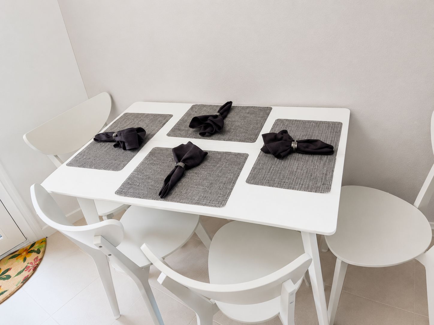 Ein weißer Tisch mit vier quadratischen Untersetzern und schwarzen, gefalteten Servietten darauf.