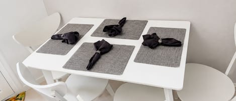 A white table with four square placemats and black napkins folded on top.