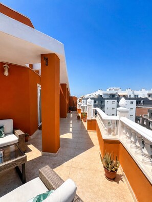 Eine Dachterrasse mit Gartenmöbeln, Topfpflanzen und Blick auf umliegende Gebäude.